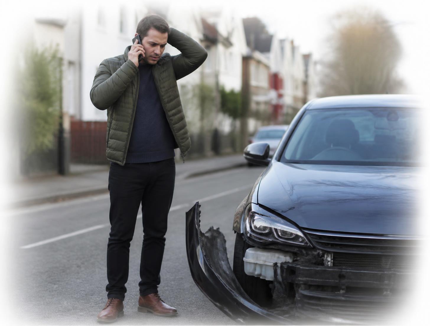 Driver on the phone beside their damaged car after an accident